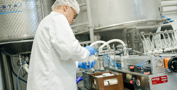 Ein Mitarbeiter füllt Joghurt in Gläser ab, verschraubt ihn händisch und stellt das Glas in einen 6er-Träger.