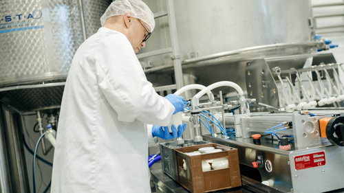 KI generiert: Mitarbeiterin in weißer Schutzkleidung arbeitet in einer Produktionshalle.