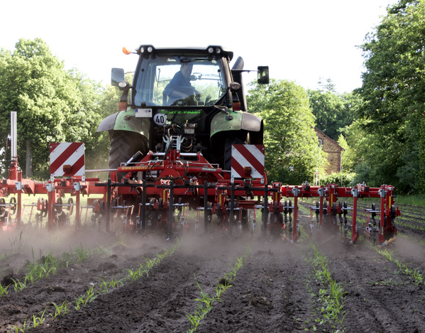 KI generiert: Ein Traktor bearbeitet ein Feld mit einer Maschine, umgeben von Bäumen.
