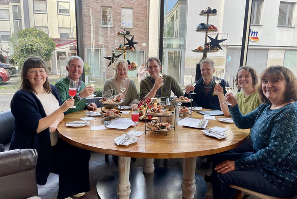 KI generiert: Eine Gruppe Menschen am Tisch stößt mit Getränken an. Einladende Atmosphäre.