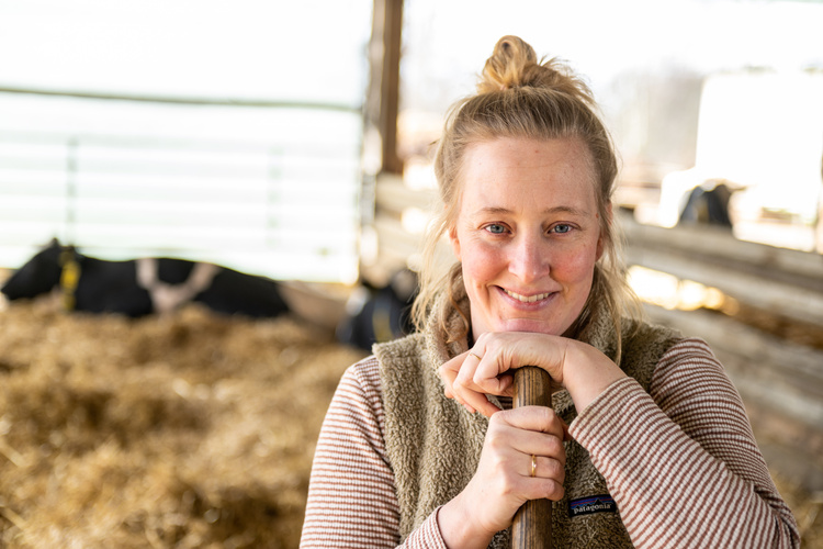 KI generiert: Eine Frau lächelt in einem Stall mit Kühen im Hintergrund.