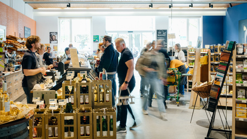 KI generiert: Das Bild zeigt einen belebten Bio-Supermarkt mit Kunden und Regalen voller Bio-Produkte.