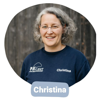 KI generiert: Eine Person mit Brille lächelt. Text auf Shirt: "Gut Wilhelmsdorf" und "Christina". Darunter: "Christina".