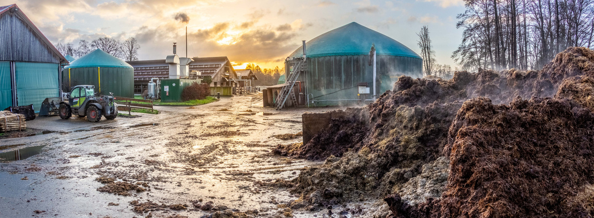KI generiert: Landwirtschaftlicher Betrieb bei Sonnenuntergang mit Misthaufen und Traktor im Vordergrund.