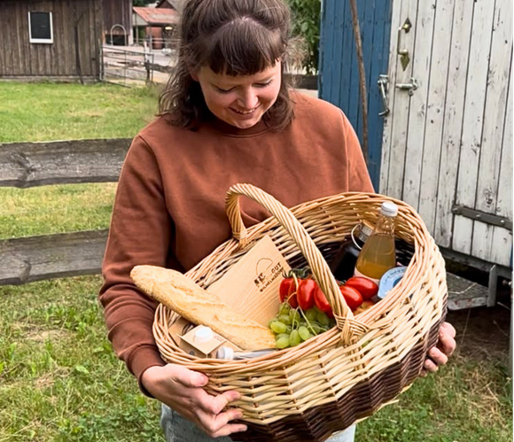 KI generiert: Eine Person hält einen Korb mit Brot, Gemüse und Getränken.