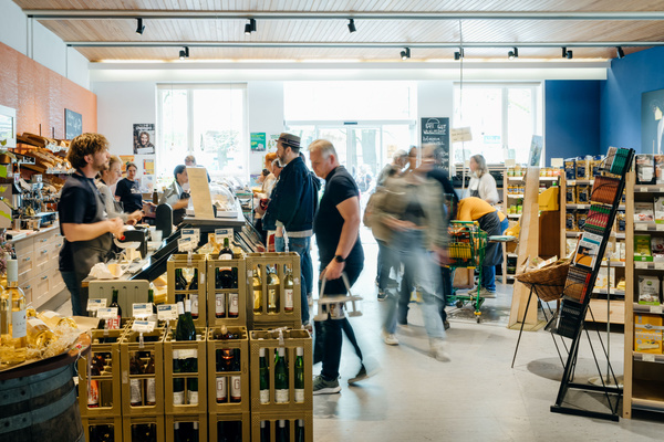 KI generiert: Menschen im gut besuchten Bioladen, mit Regalen voller Produkte, vor allem Weinflaschen.