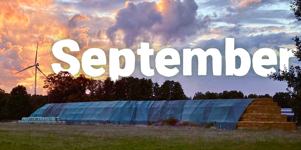 KI generiert: Landschaft mit Windrad, Heu und Bäumen bei Sonnenuntergang. Text: "September".