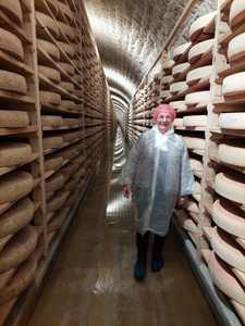 Katrin steht vor den Reiferegalen voll gefüllt mit runden Käselaiben.