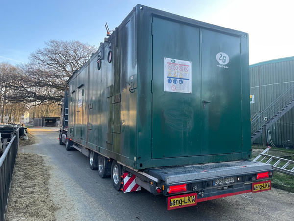 KI generiert: Ein grüner Container auf einem Anhänger, parkend auf einer Straße, mit Warnhinweisen an der Tür.