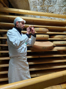 Ein Käser zeigt große Käselaibe im Reiferaum.