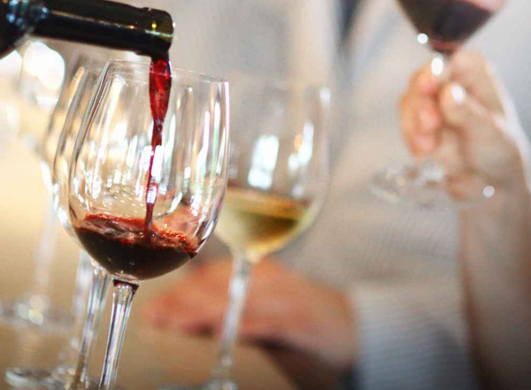 KI generiert: Rotwein wird in ein Glas gegossen, daneben stehen weitere Weingläser.