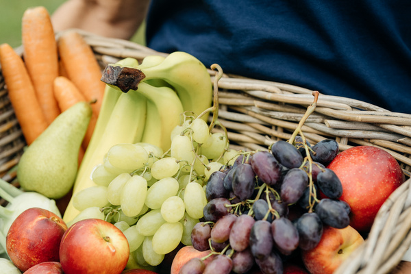KI generiert: Ein Korb voller Obst und Gemüse, darunter Bananen, Trauben, Äpfel, Birne und Karotten.