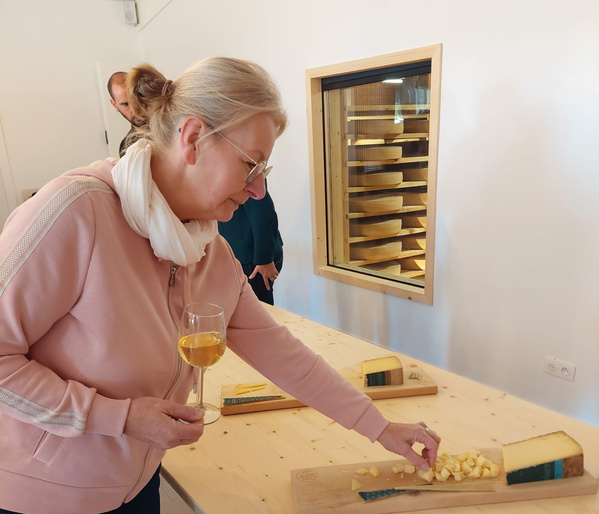 Katrin greift bei einer Käseverkostung zu einem Stück Käse und hat eine passende Weinbegleitung in der Hand.