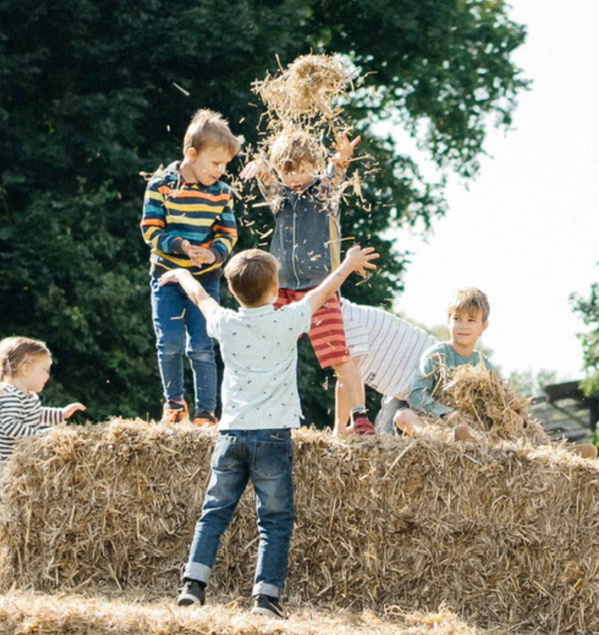 KI generiert: Kinder spielen fröhlich auf einem Strohballen im Freien.