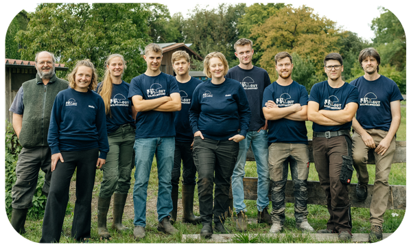 Eine Gruppe von Menschen posiert am Holzzaun der Kuhweide in blauen Gut-Wilhelmsdorf-Shirts.