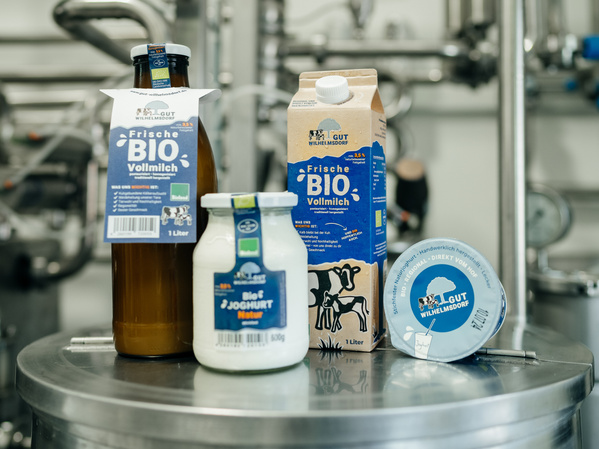 Vier Bio-Milchprodukte auf einem Edelstahl-Kessel in unserer regionalen Hofmolkerei: links ein Liter Milch in der Glasflasche, davor 500g Joghurt im Glas, rechts dahinter ein Liter Milch im Klimakarton und rechts daneben 250g Joghurt im praktischen Becher.