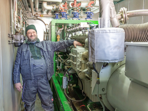 KI generiert: Ein Mann in Arbeitskleidung steht neben einer großen Maschine mit Rohren und Ventilen in einem technischen Raum.