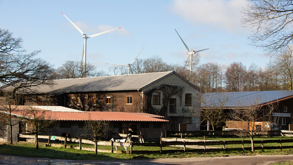 KI generiert: Ein Bauernhof mit Windrädern im Hintergrund. Auf einem Gebäude steht „Biokreis“.