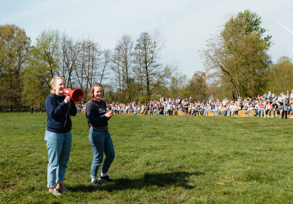 KI generiert: Zwei Frauen auf einer Wiese veranstalten ein Event mit Megafon, große Menschenmenge im Hintergrund.