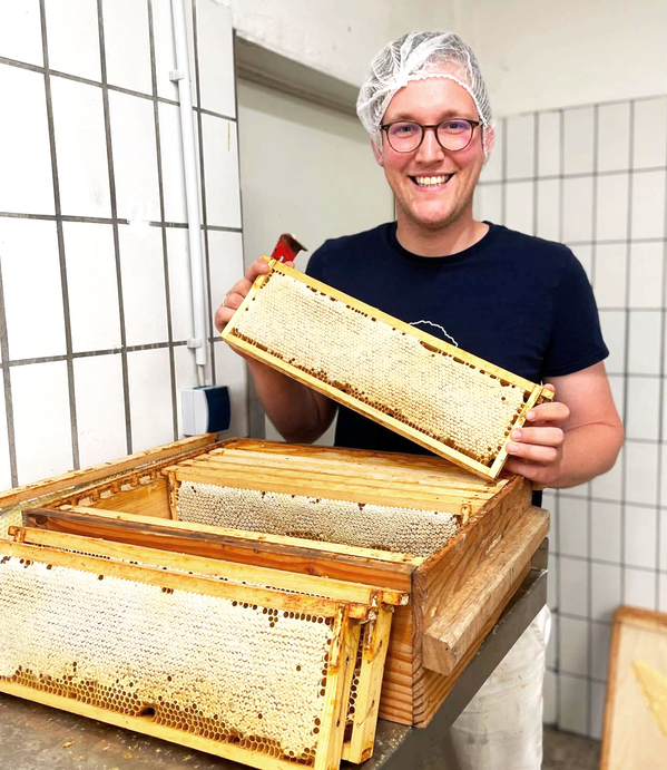KI generiert: Ein Imker hält einen Honigrahmen in der Hand und lächelt dabei.