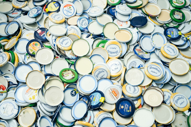 KI generiert: Ein Haufen bunter Plastikdeckel, viele mit Beschriftung. Texte: "Landliebe Joghurt", "3,5%", "fett".