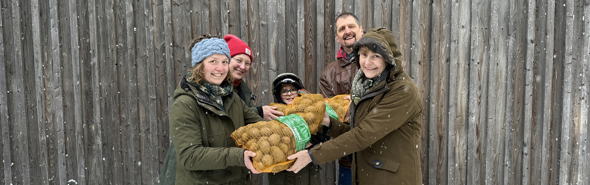 KI generiert: Eine Gruppe von Menschen hält zwei Säcke Kartoffeln vor einem Holzzaun.