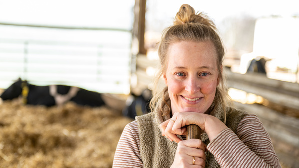 KI generiert: Eine Frau lächelt in die Kamera, im Hintergrund sind Kühe im Stall.