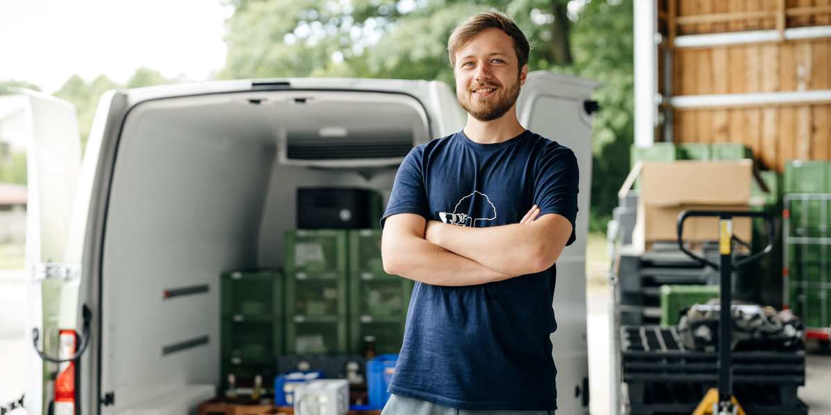 KI generiert: Ein Mann steht mit verschränkten Armen vor einem Lieferwagen mit grünen Kisten.