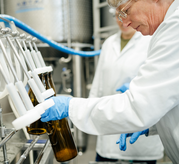Anke füllt Milch an der Flaschenabfüllmaschine in die typische, braune Gut-Wilhelmsdorf-Glasflasche.