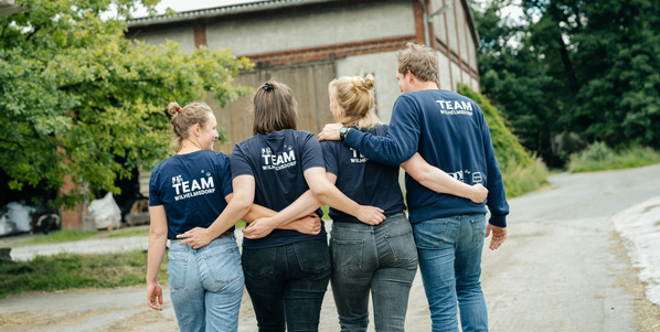 Die vier Geschäftsführer von Gut Wilhelmsdorf, Maike, Caro, Rieke und Jan, vor einer Hofkulisse im Sommer. 