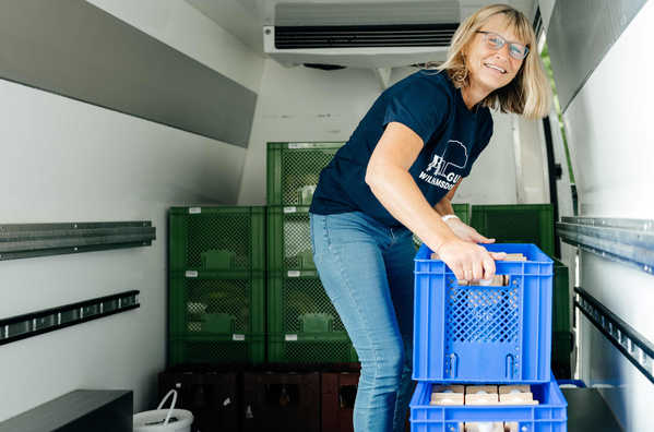 KI generiert: Eine Frau lädt blaue Kiste in einen Transporter ein.