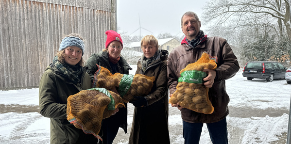 KI generiert: Vier Personen halten Kartoffelsäcke im Schnee, lächelnd in die Kamera.